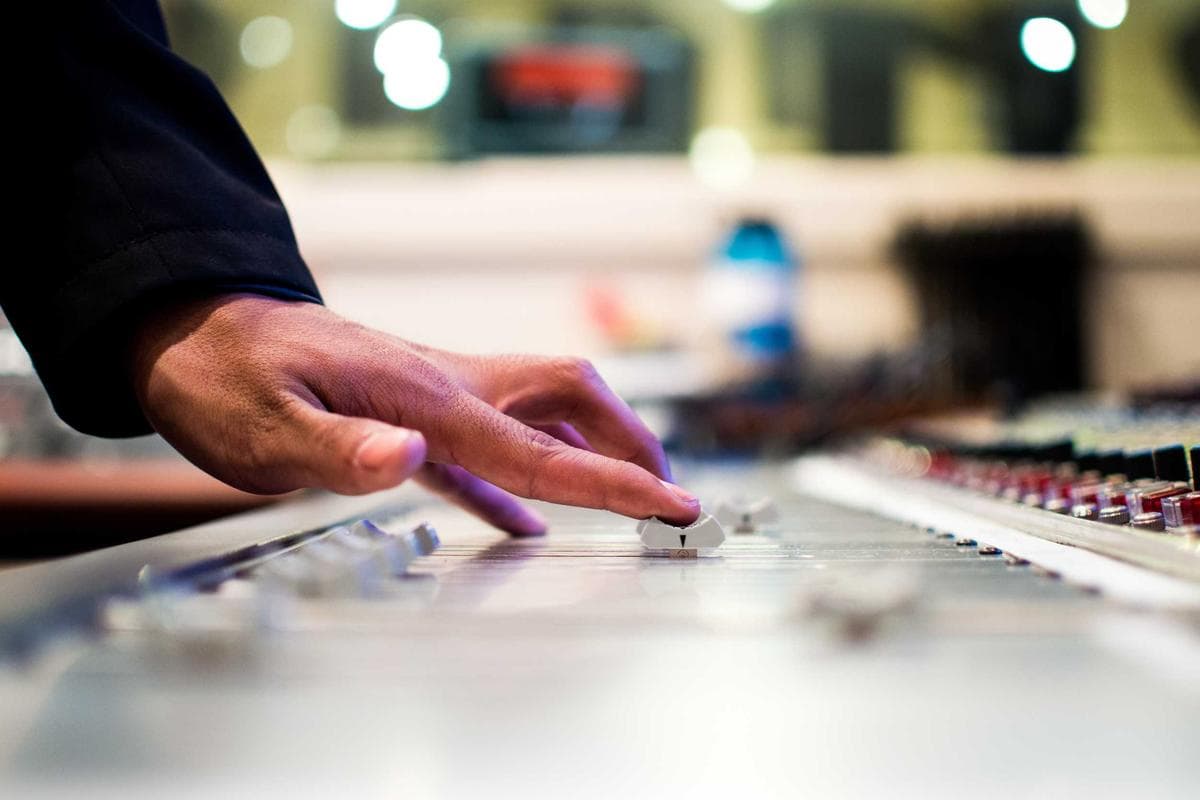 Hand on a studio mixing console with warm bokeh